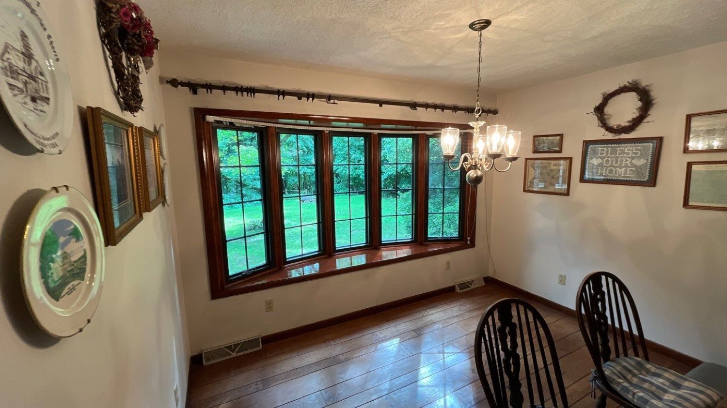 A bank of four new grid windows across a dining room wall, stained wood casing and a deep sill, lawn and trees beyond