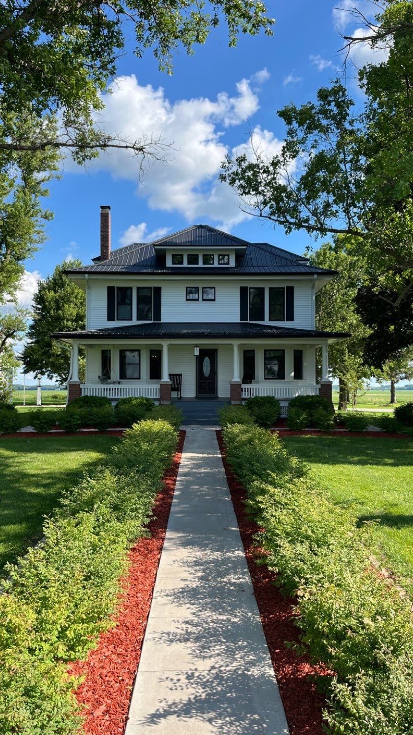 Restored white American Foursquare farmhouse with new siding, dark hipped roof, and a full front porch, seen straight on from the walkway