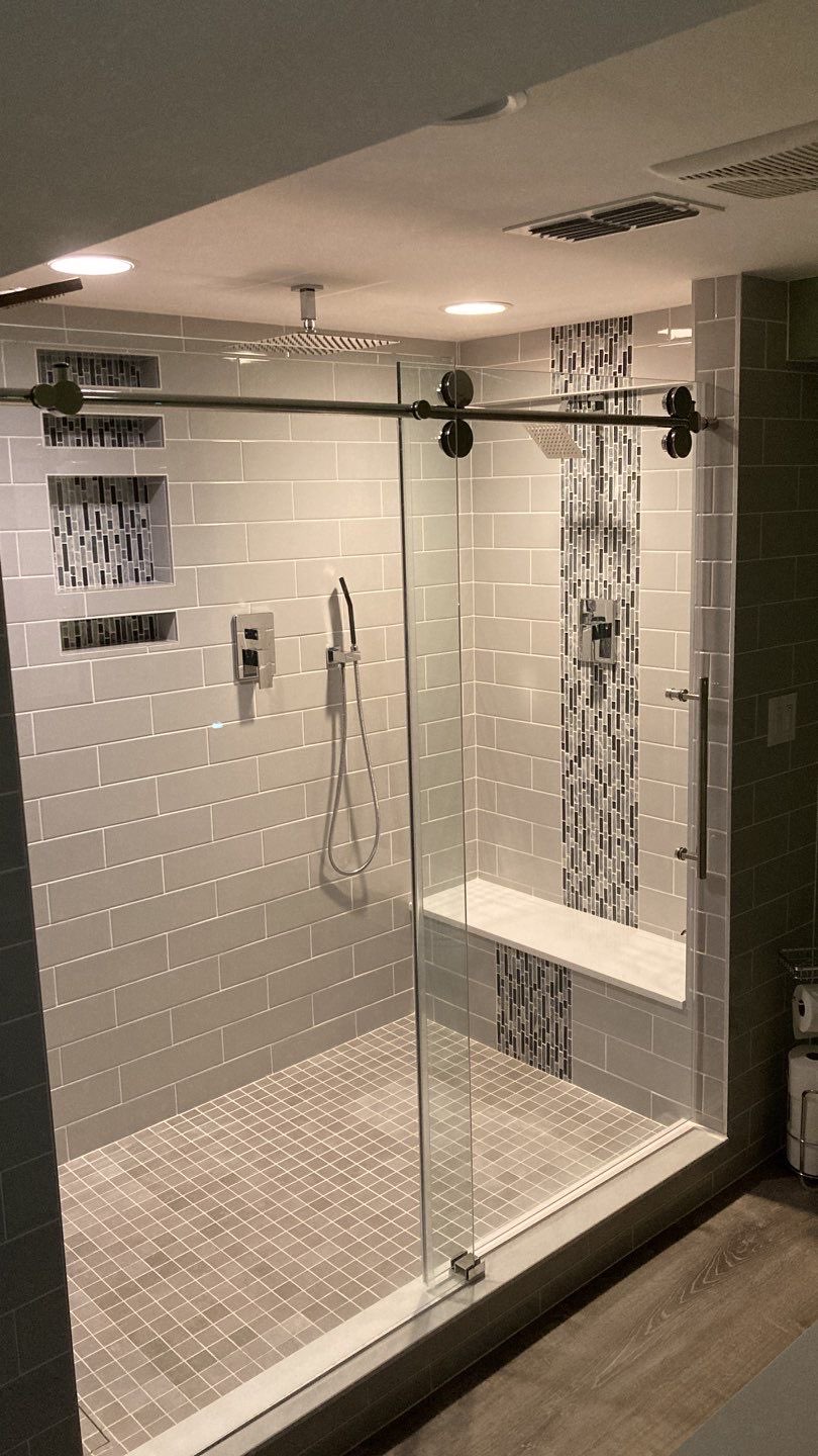 Large custom tiled shower with grey tile, vertical glass mosaic accent bands, recessed niches, a built-in bench, rain head and handheld, behind a sliding glass door