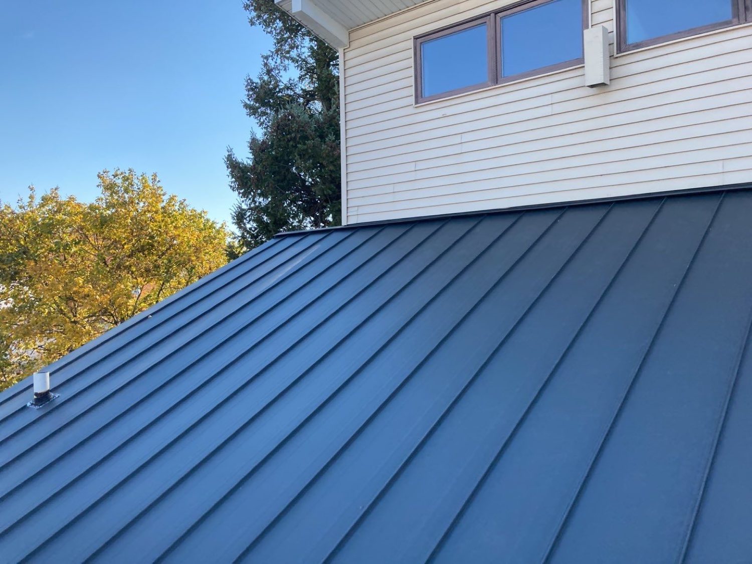 Standing-seam metal roof plane meeting a white sided wall, seams running straight down to the eave