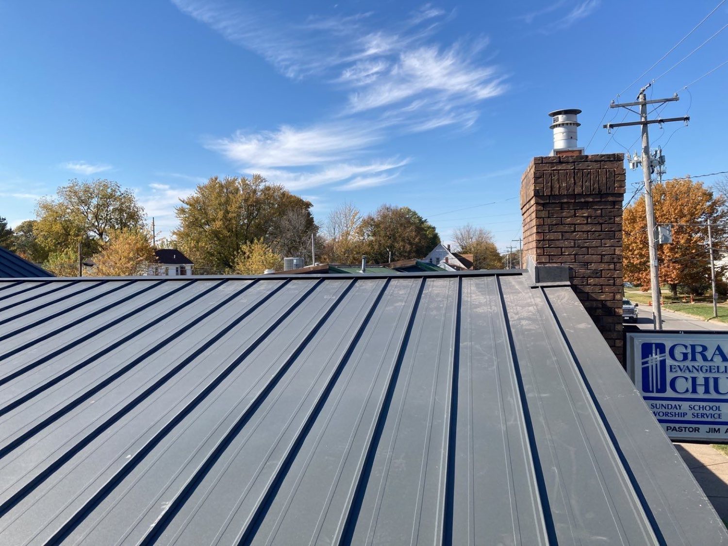 A long run of charcoal standing-seam metal roofing with tall vertical seams and no exposed fasteners, under a blue sky